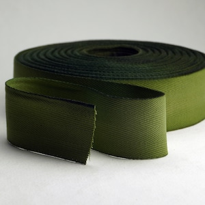 Op de afbeelding: Een rol groene keperband met een herringbone-patroon. De band is opgerold en een deel is uitgerold om de textuur te laten zien.