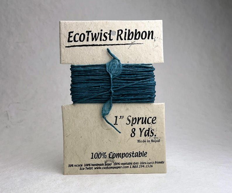 May include: A spool of dark teal EcoTwist Ribbon wrapped around a light tan paper card. The card features the text EcoTwist Ribbon, 1&rdquo; Spruce, 8 Yds., Made in Nepal, and 100% Compostable. The ribbon has a textured, twisted appearance.