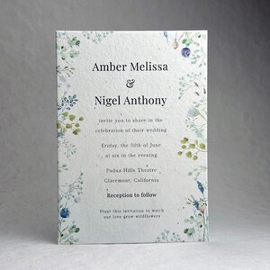 May include: A rectangular wedding invitation with floral accents. The invitation features the names "Amber Melissa & Nigel Anthony" and event details. The invitation is decorated with delicate green and blue floral illustrations.