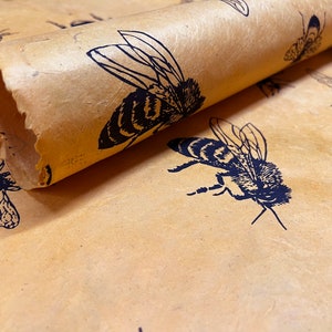 May include: A roll of brown wrapping paper with a repeating pattern of black bees. The paper has a textured, handmade look.