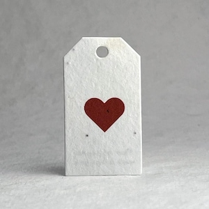 May include: A rectangular white paper tag with a textured surface and a circular hole at the top. A solid dark red heart is printed in the center of the tag. The tag has angled corners at the top and a flat bottom edge, featuring a simple design.