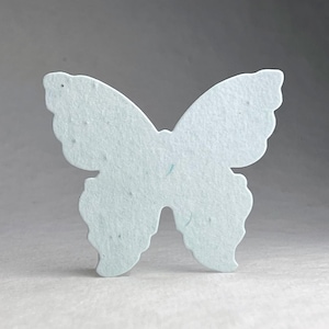 May include: A light blue butterfly-shaped decorative item. The butterfly has a symmetrical design with rounded wing edges and a textured surface. The item is likely made of paper or a similar material, and is suitable for crafts or decor.