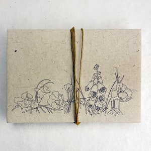 May include: A brown paper notebook with a string closure and a black line drawing of flowers on the front cover.