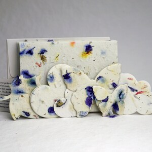 May include: A set of paper butterfly seed paper cards with a white background and blue and purple flower petals. The cards are arranged in a row, with the largest card in the back and the smallest card in the front. The cards are made of recycled paper and are biodegradable.