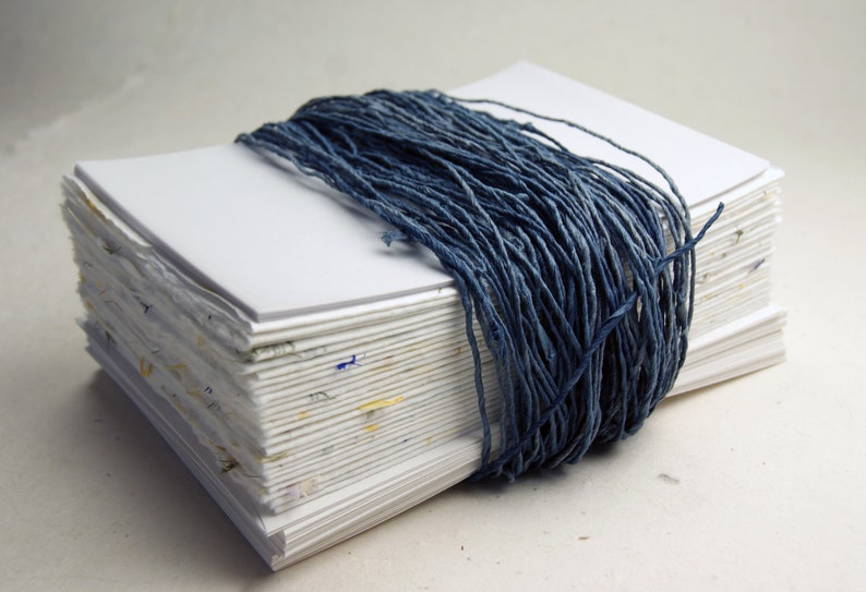 May include: A stack of white paper pages bound together with a thick blue cord. The pages are slightly rough and have a handmade look.