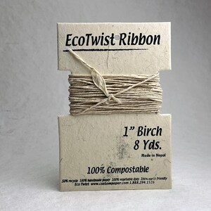May include: A spool of EcoTwist Ribbon in a light beige color, wrapped around a rectangular card made of textured paper. The card features the text EcoTwist Ribbon, 1 inch Birch, 8 Yds., Made in Nepal, and 100% Compostable in black ink.
