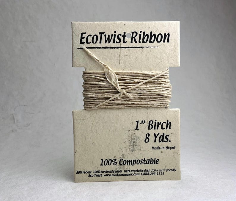 May include: A spool of EcoTwist Ribbon in a light beige color, wrapped around a rectangular card made of textured paper. The card features the text EcoTwist Ribbon, 1 inch Birch, 8 Yds., Made in Nepal, and 100% Compostable in black ink.