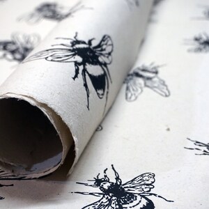 May include: A roll of white wrapping paper with a black and white bee pattern. The paper is rolled up and the end is visible.