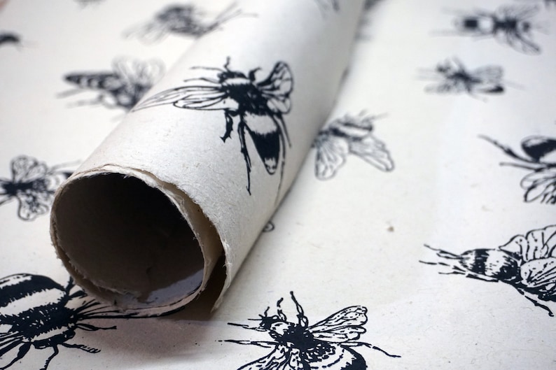 May include: A roll of white wrapping paper with a black and white bee pattern. The paper is rolled up and the end is visible.