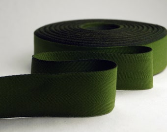 May include: A roll of dark green twill tape with a herringbone pattern. The tape is rolled up and a portion of the tape is unrolled, showing the texture of the fabric.