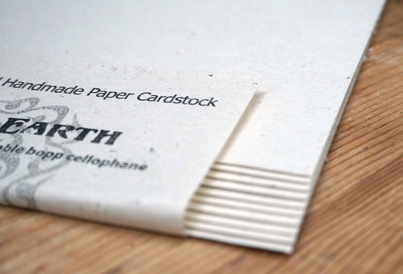 May include: A stack of white cardstock paper with the text "Handmade Paper Cardstock" and "EARTH" printed on the top sheet. The paper is wrapped in a white paper band.