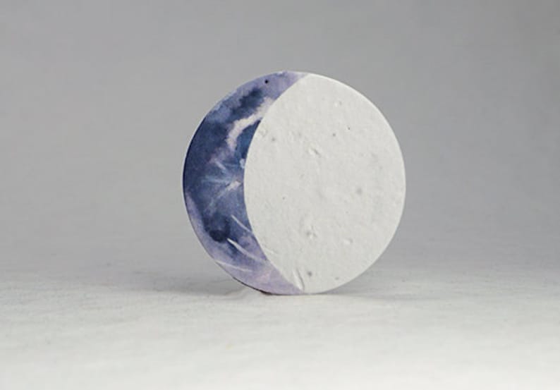 Pu&ograve; includere: Un oggetto decorativo rotondo con un design a mezzaluna. La superficie della luna &egrave; divisa, con una met&agrave; che presenta un lavaggio ad acquerello nei toni del blu e del viola, e l'altra met&agrave; &egrave; bianca e strutturata. L'oggetto &egrave; su uno sfondo neutro.
