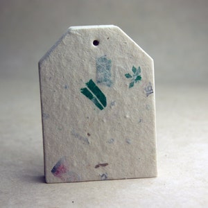 May include: A rectangular, off-white gift tag with a small hole at the top. The tag has a textured surface with flecks of color and green botanical illustrations. The tag is blank, ready for personalization.