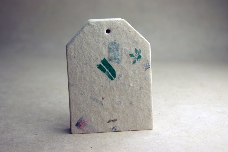 May include: A rectangular, off-white gift tag with a small hole at the top. The tag has a textured surface with flecks of color and green botanical illustrations. The tag is blank, ready for personalization.