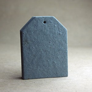 May include: A gray, tag-shaped object with a textured surface and a small hole at the top. The tag has a rectangular body with a slightly angled top, and it stands against a neutral background.