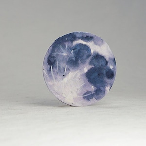 Pu&ograve; includere: Un dipinto rotondo ad acquerello della luna. La luna &egrave; raffigurata in tonalit&agrave; di blu e viola, con riflessi bianchi. L'opera d'arte &egrave; su uno sfondo bianco.
