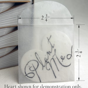 May include: A clear heart-shaped envelope with a white heart inside. The heart has the words "Planted" and "Married" written on it. The envelope is 2 3/4 inches wide and 2 3/4 inches tall.