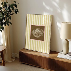 a green and white striped poster has a brown square with a pink border. In the square is a vintage white conch seashell image. The print is minimalist, beachy, with an east coast aesthetic. Great for bedroom or bathroom decor.