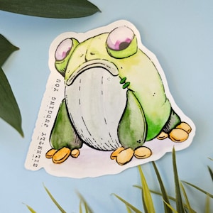 May include: A sticker featuring a cartoon frog with a grumpy expression. The frog is primarily green and white with yellow accents. Text on the left side reads "SILENTLY JUDGING YOU". The background is light blue with green foliage.