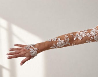 May include: A sheer, long sleeve glove featuring intricate white floral lace embroidery that extends from the upper arm down to the wrist, with a delicate lace attachment that loops around the middle finger, creating a detailed botanical pattern.