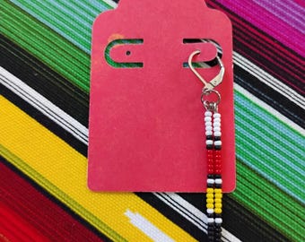 May include: A single dangle earring featuring two vertical strands of small seed beads in a repeating pattern of white, black, red, white, yellow, and black, attached to a silver-toned metal leverback hook and displayed on a red card.