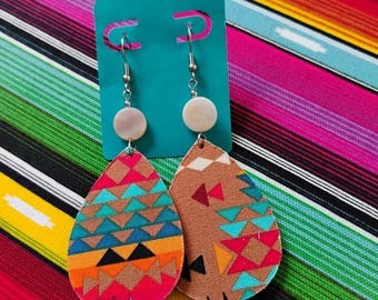 May include: A pair of teardrop-shaped earrings attached to a teal display card. Each earring features a round white bead at the top and a fabric pendant with a geometric pattern in shades of brown, bright pink, orange, and turquoise blue.