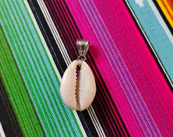 May include: A cowrie shell pendant featuring a smooth, off-white, oval-shaped shell with a central serrated opening. The shell is attached to a polished silver-toned metal bail at the top, designed for suspension on a chain or cord.