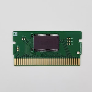 May include: A green circuit board with gold connectors and a dark purple central processor. The board has the text "Re" and other markings, including "ACB-E01 ReBoard". The board is rectangular with a notched edge.