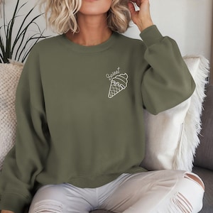 Op de afbeelding: Een groen sweatshirt met een witte omtrek van een ijshoorn en het woord "Sweet" erboven.