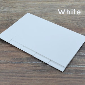 May include: White blank card with a folded edge and four creases. The card is lying on a wood surface.