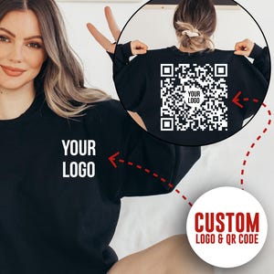 Peut inclure: Sweat-shirt noir avec le texte "YOUR LOGO" sur le devant. Le dos du sweat-shirt présente un code QR avec le texte "YOUR LOGO" au centre. L'image comprend également le texte "CUSTOM LOGO & QR CODE".