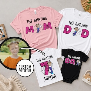 May include: A collection of four garments including a pink t-shirt with text THE AMAZING MOM, a white t-shirt with text THE AMAZING DAD, a white t-shirt with text THE AMAZING SOPHIA, and a black bodysuit with text THE AMAZING BRO, all featuring spiderweb graphics.