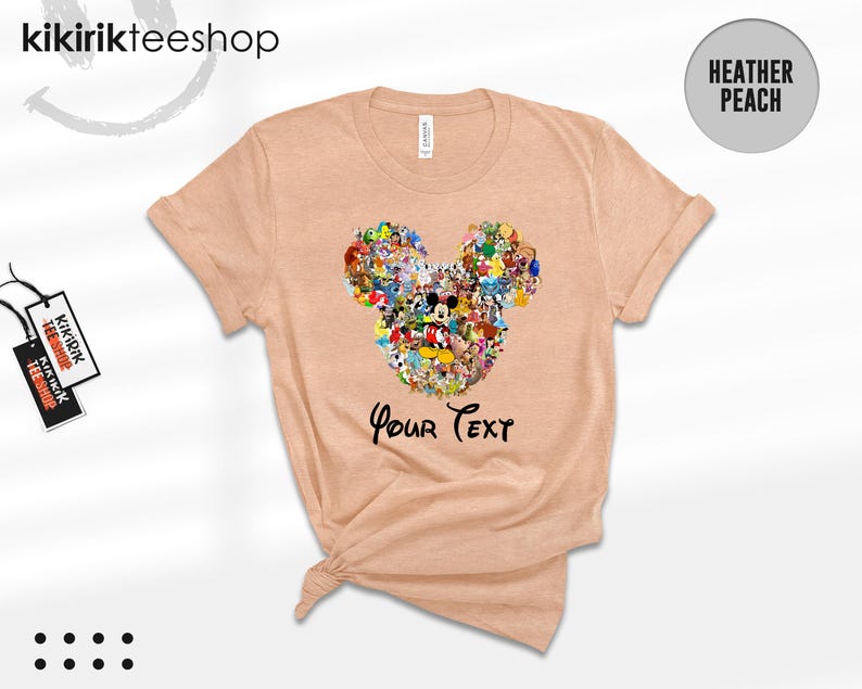 Pu&ograve; includere: T-shirt color pesca con un design a forma di testa di Topolino composto da vari personaggi dei cartoni animati. Il testo "Your Text" &egrave; stampato sotto. La maglietta ha le maniche arrotolate e un'etichetta "Kikirikteeshop".