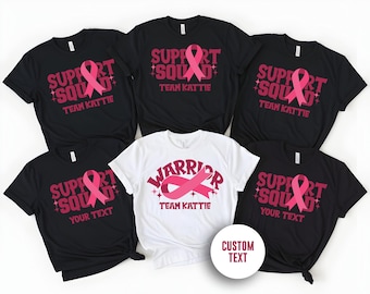May include: Set of six black t-shirts with pink ribbon designs. The shirts have the text "Support Squad" and "Team Kattie" on them. One shirt has the text "Warrior" and "Team Kattie". One shirt has the text "Support Squad" and "Your Text".