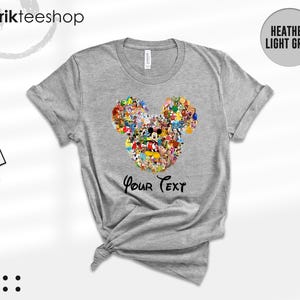 Pu&ograve; includere: T-shirt grigio melange con un design a forma di testa di Topolino composto da vari personaggi dei cartoni animati. Le parole "Your Text" sono stampate sotto. La maglietta ha maniche corte e girocollo.