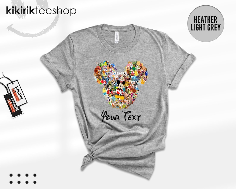 Pu&ograve; includere: T-shirt grigio melange con un design a forma di testa di Topolino composto da vari personaggi dei cartoni animati. Le parole "Your Text" sono stampate sotto. La maglietta ha maniche corte e girocollo.