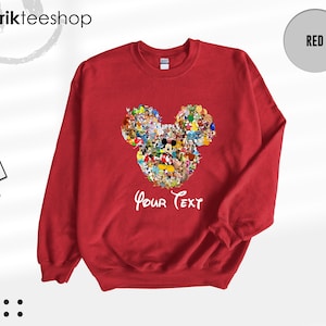 Pu&ograve; includere: Una felpa rossa con un disegno della testa di Topolino composto da vari personaggi dei cartoni animati. Le parole "Your Text" sono scritte in bianco sotto. La felpa ha maniche lunghe e girocollo.