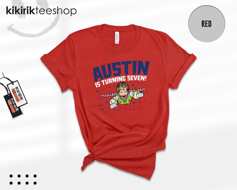 K&ouml;nnte beinhalten: Ein rotes Kurzarm-T-Shirt mit einer Grafik eines Kindes in einem Weltraum-Ranger-Kost&uuml;m mit Fl&uuml;geln. Der Text AUSTIN IS TURNING SEVEN! ist in blauen und wei&szlig;en Buchstaben gedruckt, umgeben von kleinen blauen Sternen. Ein Markenetikett ist befestigt.