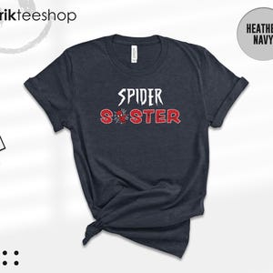 Puede incluir: Camiseta azul marino jaspeado con las palabras "SPIDER SISTER" en letras blancas y rojas. Un gr&aacute;fico de telara&ntilde;a est&aacute; entre las palabras. La camiseta es de Kikirikiteeshop.