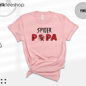 Puede incluir: Una camiseta rosa claro con las palabras "SPIDER PA" en negro y rojo, con una telara&ntilde;a y un gr&aacute;fico de ara&ntilde;a. La camiseta es de la marca "Kikirikteeshop".