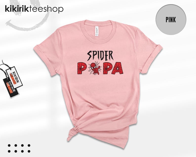 Puede incluir: Una camiseta rosa claro con las palabras "SPIDER PA" en negro y rojo, con una telara&ntilde;a y un gr&aacute;fico de ara&ntilde;a. La camiseta es de la marca "Kikirikteeshop".