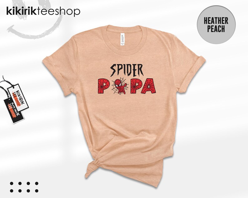 Puede incluir: Camiseta color melocot&oacute;n jaspeado con las palabras "SPIDER PA" en negro y rojo. La palabra "SPIDER" est&aacute; en una fuente estilizada, y "PA" est&aacute; en negrita, fuente roja con un dise&ntilde;o de telara&ntilde;a. La camiseta tiene mangas cortas y cuello redondo.