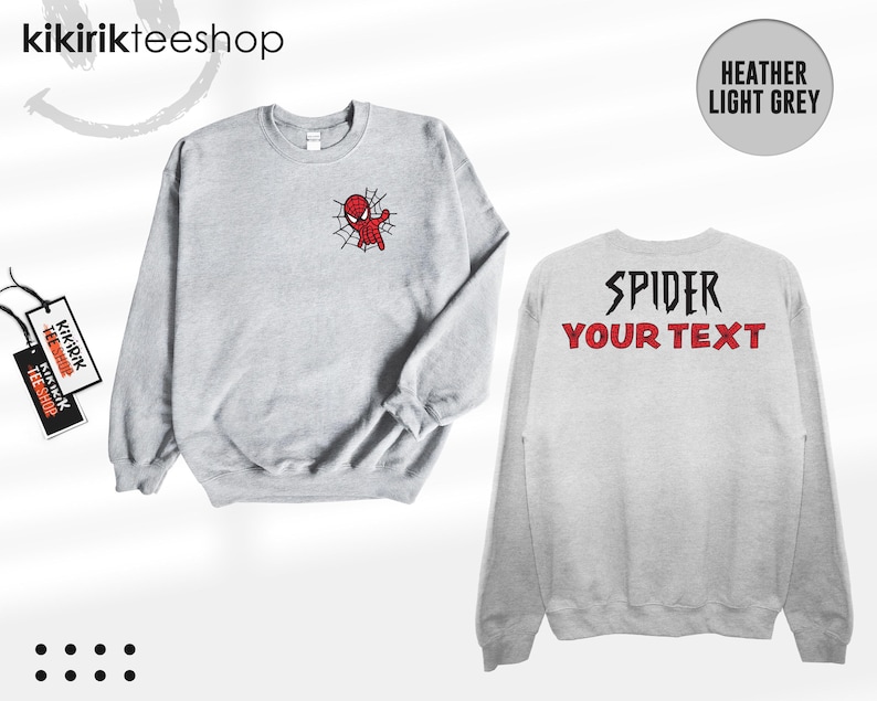 May include: A heather light grey crewneck sweatshirt featuring a small red and black spider-themed character graphic on the front left chest. The back of the sweatshirt displays the black text SPIDER and the red text YOUR TEXT in a bold font.