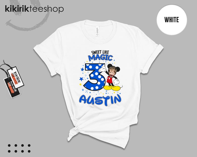 May include: A white short-sleeve t-shirt featuring a graphic print with the text SWEET LIKE MAGIC, the number 3 in blue with white polka dots, and the name AUSTIN. A cartoon character with a child's face is positioned next to the number 3.
