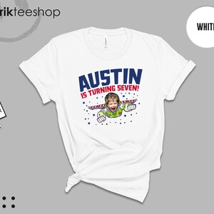 K&ouml;nnte beinhalten: Ein wei&szlig;es T-Shirt mit einem Grafikdruck, der das Gesicht eines Kindes auf dem K&ouml;rper einer Weltraumfigur mit Fl&uuml;geln zeigt. Der Text AUSTIN IS TURNING SEVEN! ist in blauen und roten Buchstaben gedruckt, umgeben von kleinen blauen Sternsymbolen.