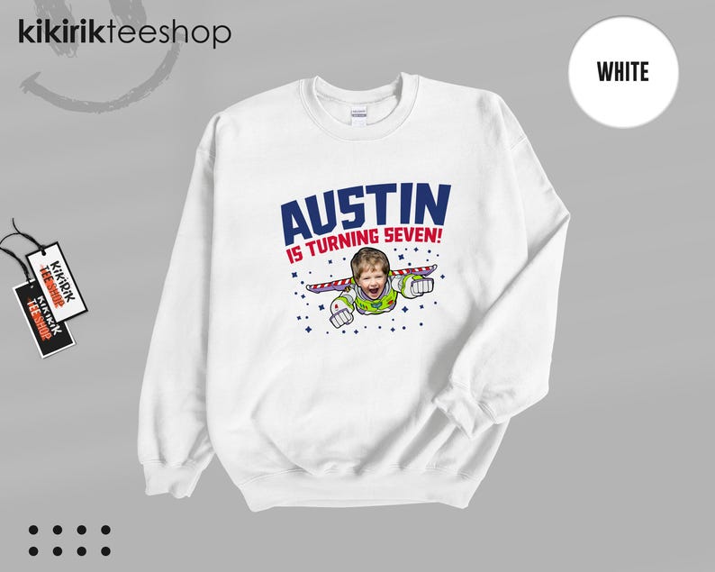K&ouml;nnte beinhalten: Ein wei&szlig;es Sweatshirt mit Rundhalsausschnitt und einem Grafikdruck, der das Gesicht eines Kindes auf dem K&ouml;rper einer Weltraum-Ranger-Figur zeigt. Der Text AUSTIN IS TURNING SEVEN! steht in blauen und roten Buchstaben, umgeben von kleinen blauen Sternen.