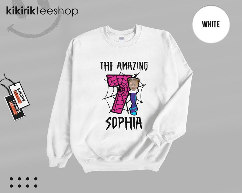 May include: A white crewneck sweatshirt featuring a graphic print of a large pink number seven with a black spiderweb pattern. The text THE AMAZING SOPHIA is printed in black above and below the number, with a small photo of a child's face.