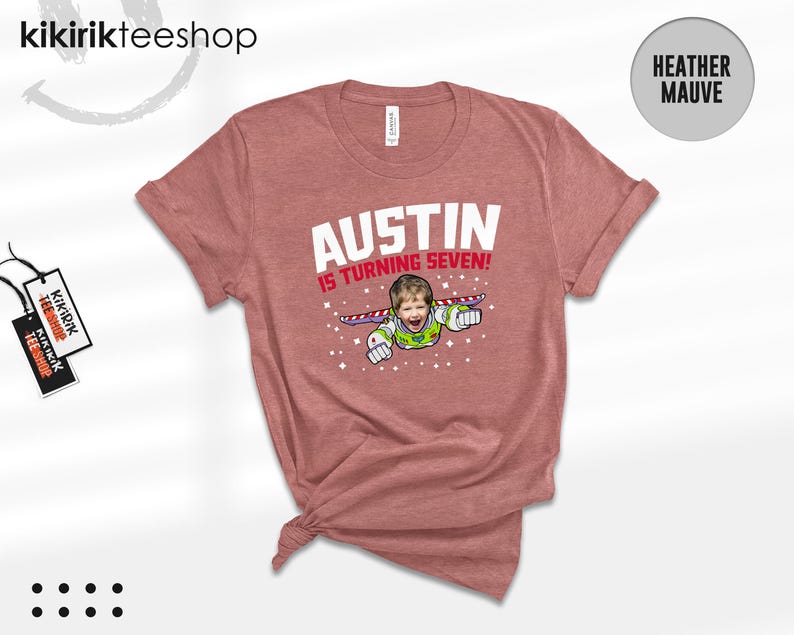 K&ouml;nnte beinhalten: Ein kurz&auml;rmeliges T-Shirt in Heather Mauve mit einer Grafik eines Kindes, das als Weltraum-Ranger mit Fl&uuml;geln verkleidet ist. Der Text AUSTIN IS TURNING SEVEN! steht in wei&szlig;er und roter Schrift, umgeben von kleinen wei&szlig;en Sternen auf der Vorderseite.