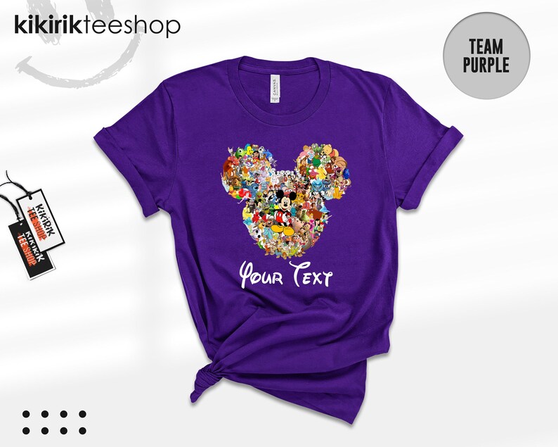 Pu&ograve; includere: Una maglietta viola con un design a forma di testa di Topolino composto da vari personaggi dei cartoni animati. La maglietta ha le maniche arrotolate e la scritta "Your Text" in bianco. Il marchio "kikirikteeshop" &egrave; visibile in alto.