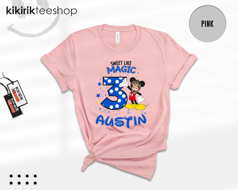 May include: A light pink t-shirt featuring a graphic with the text SWEET LIKE MAGIC, the number 3 in blue with white polka dots, and the name AUSTIN. A cartoon character with a child's face is positioned next to the number 3.